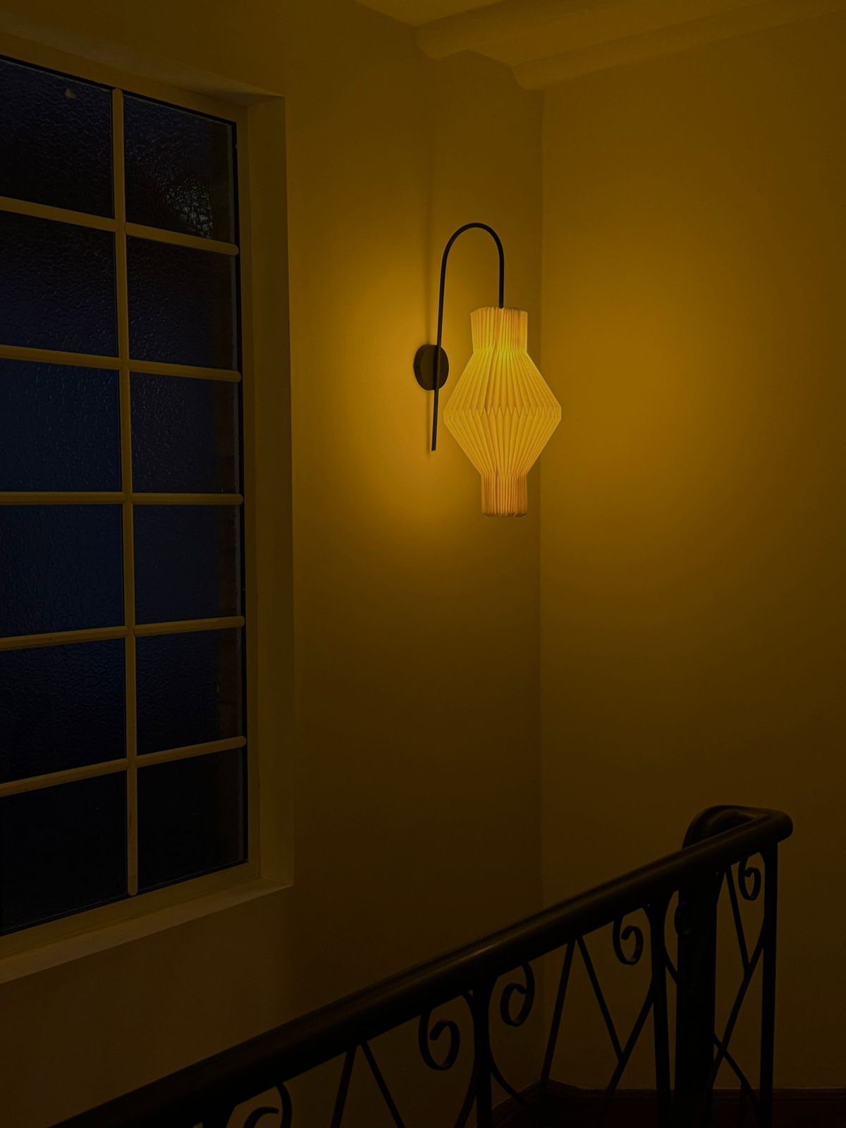 Plié Lights_Lampara de pared_aplique de pared_Fotografía de producto_Diseño geometrico_Hechas en papale doblada_con manos colombianas._Fotografía nocturna en sitio en unas escaleras, se veuna ventana al lado._Caperuza referencia Hydra