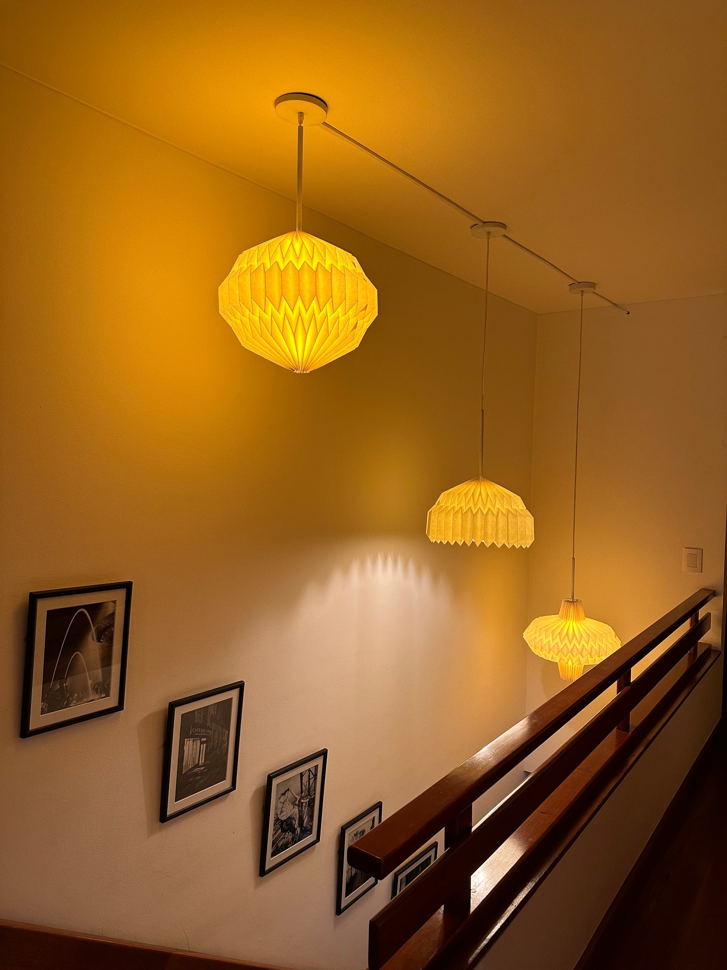 Plié Lights_Lámparas colgantes de colombia_Referencia_Orión_Alfa y antares. Las lámparas están colgante encima de una escalera, puestas escalonadamente en la misma dirección de la escalera. Las lámparas están prendidas. La lámpara Alfa está ubicada en el centro.