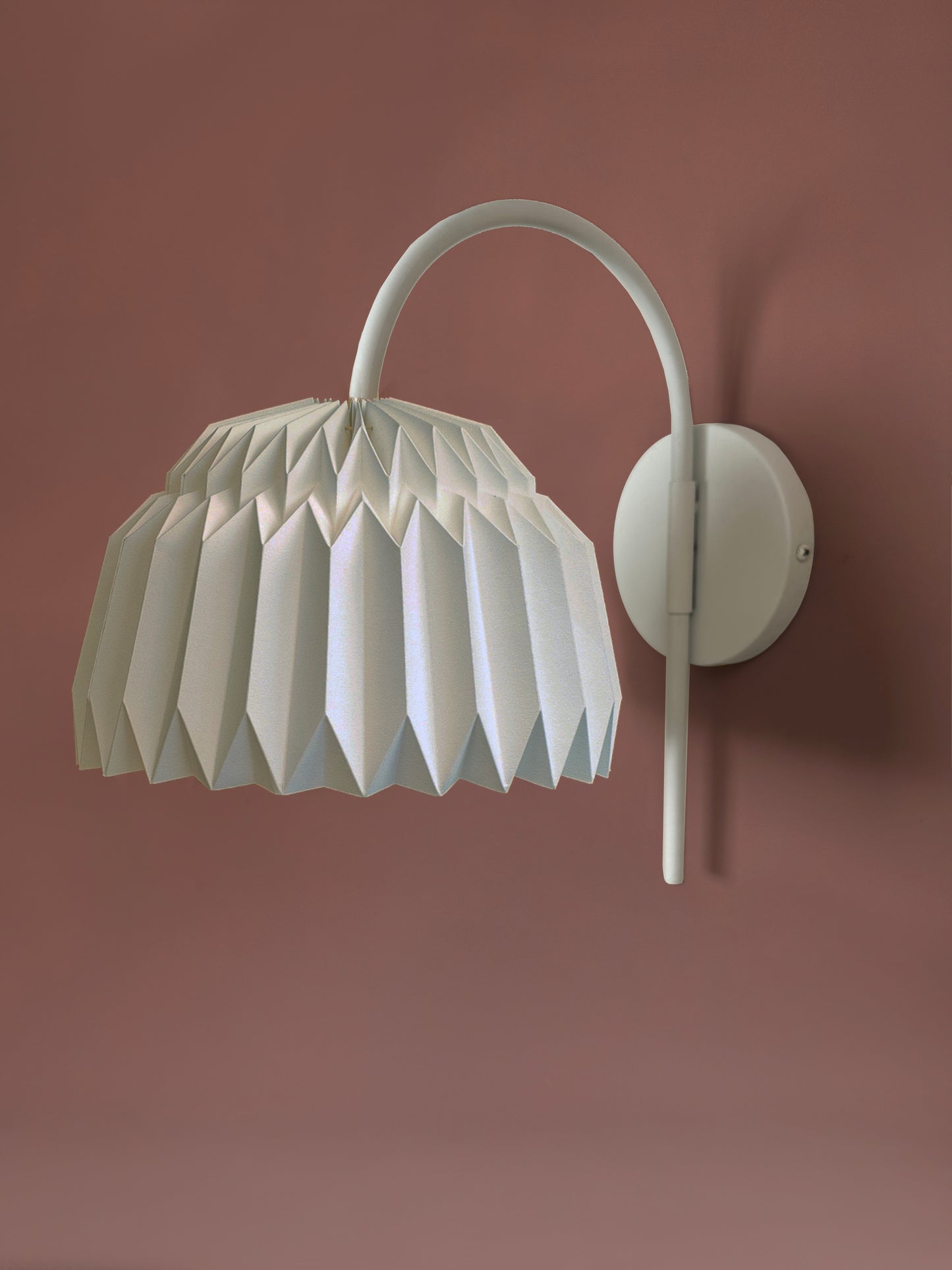 Lámpara de pared Plie Lights. Iluminación para poner en la pared, con un soporte metálico negro. La caperuza está hecha en papel, doblada a mano. Producto hecho en Colombia. Soporte metálico color blanco. Iluminación perfecta para la mesa de noche.