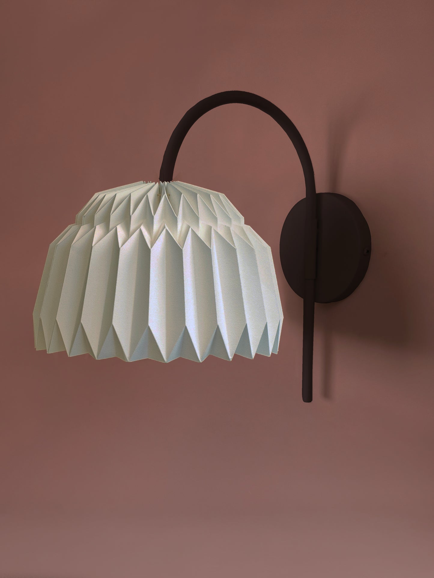 Lámpara de pared Plie Lights. Iluminación para poner en la pared, con un soporte metálico negro. La caperuza está hecha en papel, doblada a mano. Producto hecho en Colombia. Soporte metálico color negro.