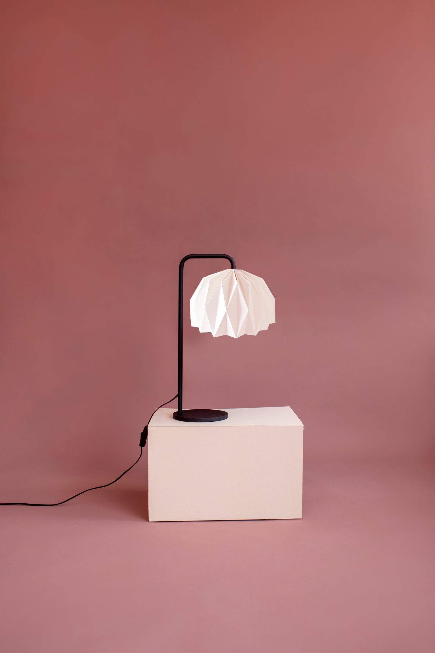 Plié Lights, lámpara hechas en colombia. Lámpara de mesa de con caperuza referencia Fenix. Caperuza en origami doblada a mano en Colombia. Estructura metálica negra.