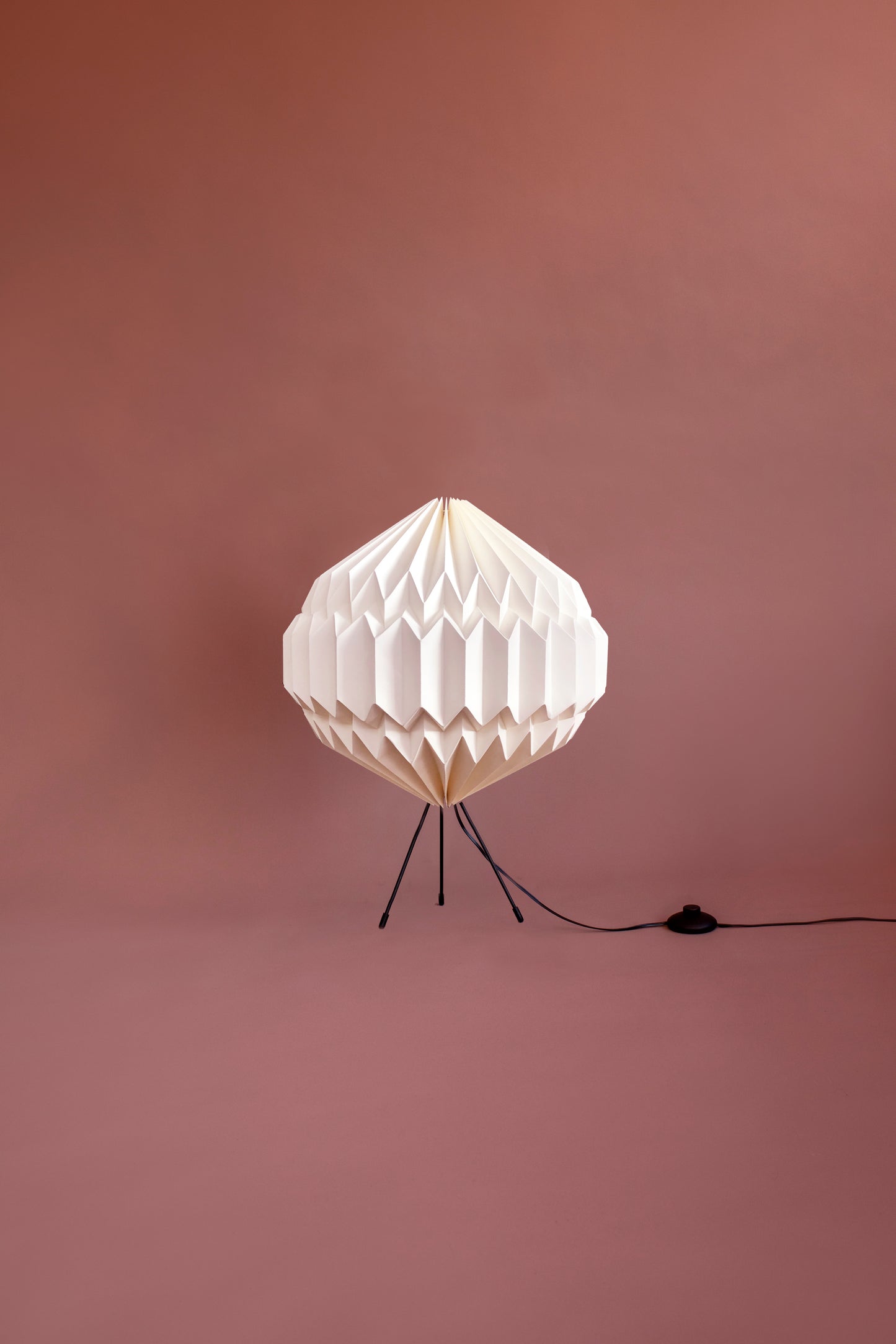 Plié Lights_Lámparas hechas a mano en Colombia, caperuza o pantallada referencia Luna, hecho a mano con papel plegado, técnica de origami. Tiene tres patas metálicas negras y cable negro. Iluminación para mesas o lámparas de piso con altura de 60 centimetros de alto. Iluminación cálida para el hogar.