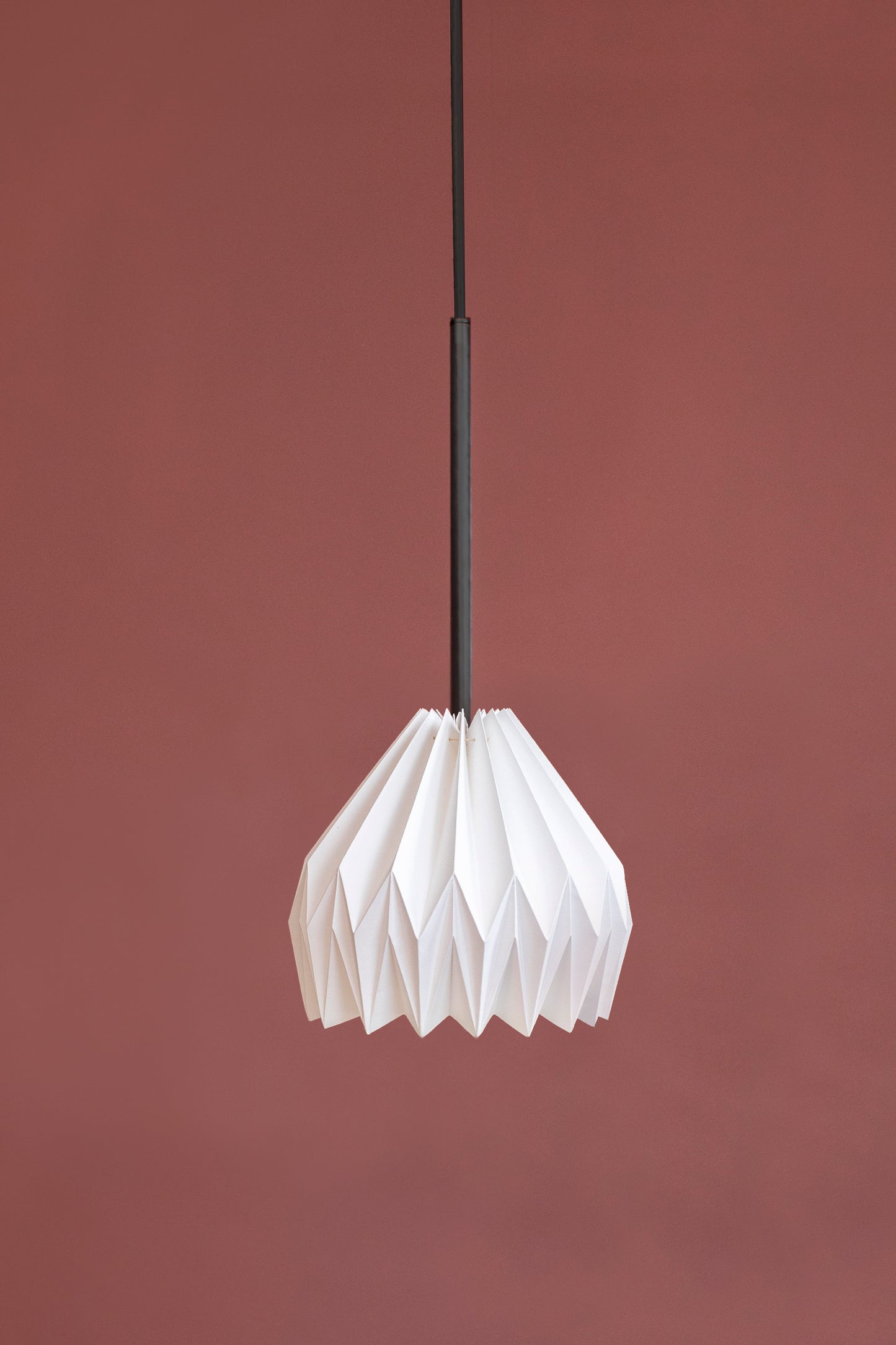 Lámpara colgante de Colombia. Plié Lights, referencia Gemini. Fotogragía de producto sobre un fondo de color rosa. Caperuza escultórica con diseño geométrico hecha en papel a mano.