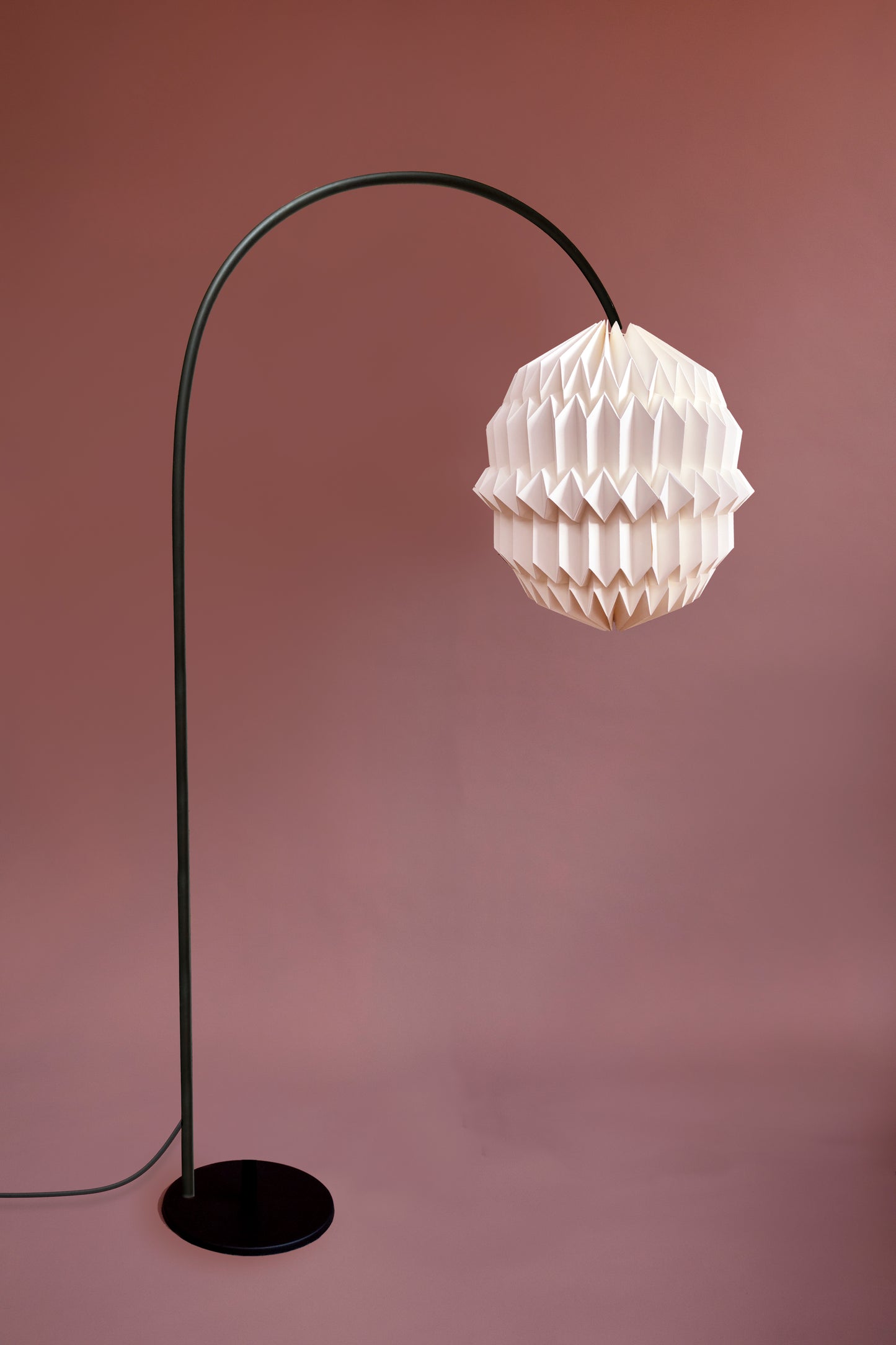Lámpara de piso Plié Lights. Esta lámparas hechas en Colombia es una fotorafía de producto. La lámpara tiene una base metálica color negro y tiene una forma en arco, lo que permite crear el efecto de una lámpara colgante pero con una base de piso. Perfecta para espacios donde uno quiere una lámpara de techo pero no tiene dónde colgarla.