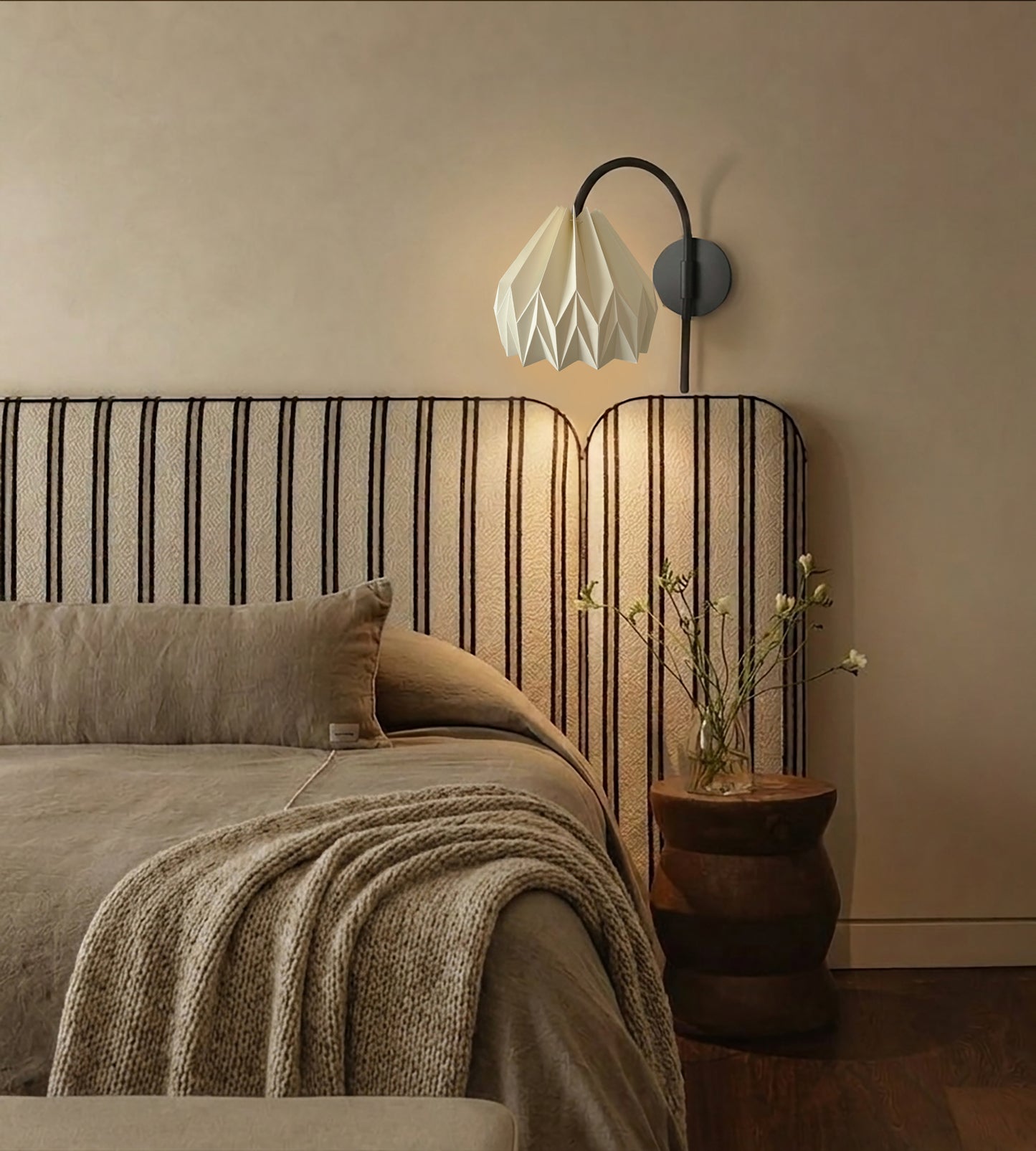 Plié Lights_Lámpara de pared ó aplique de pared referencia Gemini. Fotografía tomada en sitio de una habitación con una cama con cabecero en tela, el espacio está iluminado y la lámpara está apagada. Lámpara en papel con figura geometrica. 