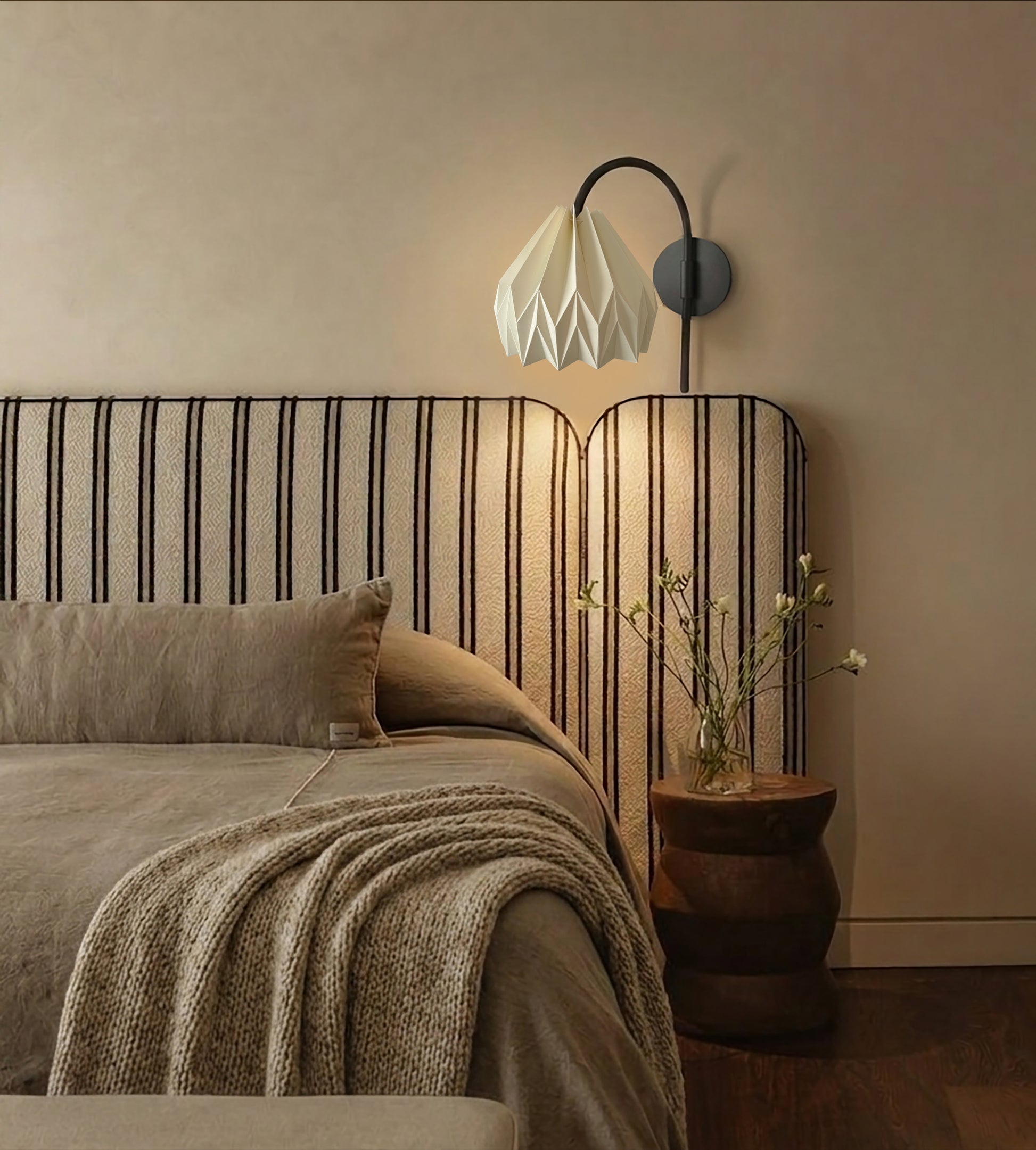 Plié Lights_Lámpara de pared ó aplique de pared referencia Gemini. Fotografía tomada en sitio de una habitación con una cama con cabecero en tela, el espacio está iluminado y la lámpara está apagada. Lámpara en papel con figura geometrica. 