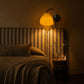 Plié Lights_Lámpara de pared ó aplique de pared referencia Gemini. Fotografía tomada en sitio de una habitación con una cama con cabecero en tela, el espacio está oscuro y la lámpara genera una luz cálida en el ambiente. 