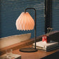 Plié Lights_Lámparas de mesa hechas en Colombia_Caperuzas con diseños geométricos hechas con papel Referencia de la caperuza Gemini. Fotografía de producto puesta encima de una consola, a los lados unos libros, un baso y un florero. La escena es de día.