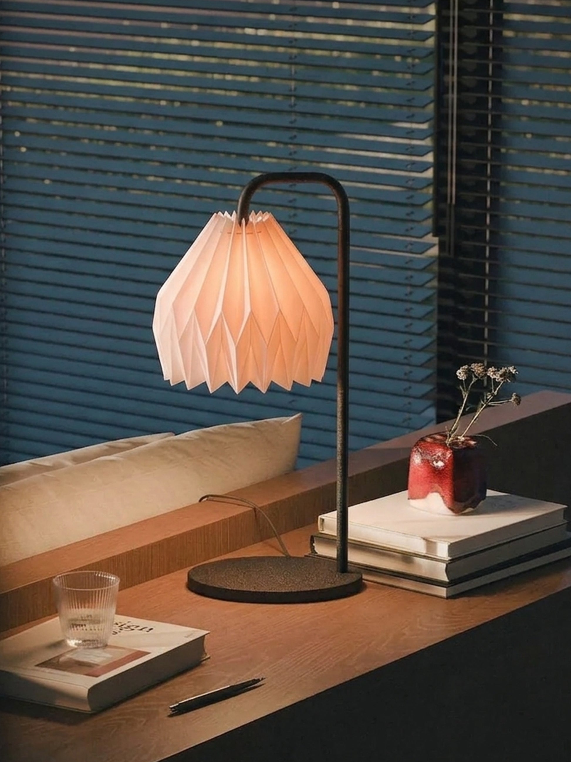 Plié Lights_Lámparas de mesa hechas en Colombia_Caperuzas con diseños geométricos hechas con papel Referencia de la caperuza Gemini. Fotografía de producto puesta encima de una consola, a los lados unos libros, un baso y un florero. La escena es de día.