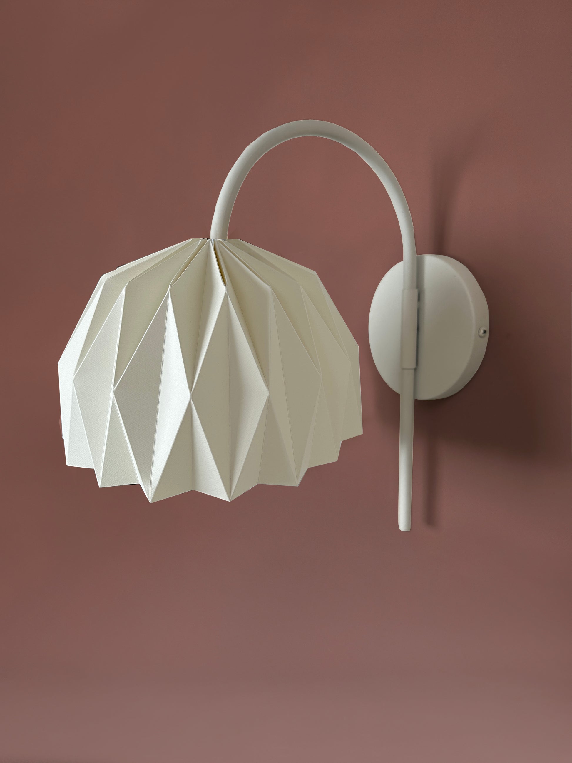 Plie Lights, lámparas hechas en Colombia a mano, por artesanos colombianos. La caperuza es de papel doblado a mano con un diseño geometrico. Soporte metálico color blanco. Perfectas para iluminar habitaciones y mesas de noche. Referencia Fenix. 