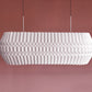 Lámpara colgante de Colombia. Plié Lights, referencia  Tauro, un fondo de color rosa. Caperuza escultórica con diseño geométrico rectangular con ángulos redondeados. El diseño genera luz directa hacia arriba y hacia abajo. Hecha en papel a mano. La base metálica es color nblanco y cable guaya.
